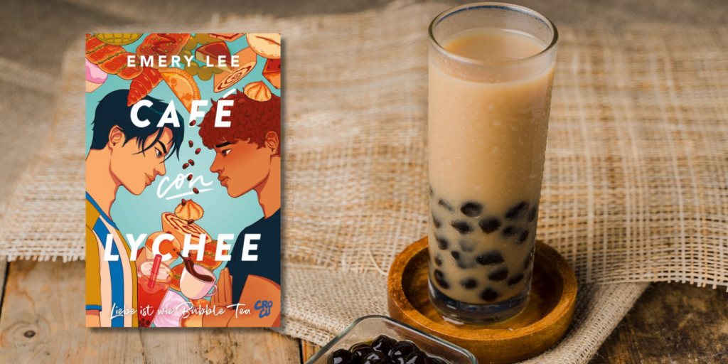 Das Buch Café con Lychee vor einem Hintergrund aus verschiedenen Jute-Stoffen auf einer alten Holzplatte, darauf ein Bubble Tea mit Milch auf einem Holz-Untersetzer.